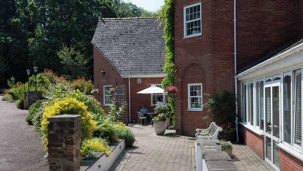 A brick building with a garden patio, outdoor seating, and a white umbrella. - Fox & Hounds Country Hotel (Chulmleigh)