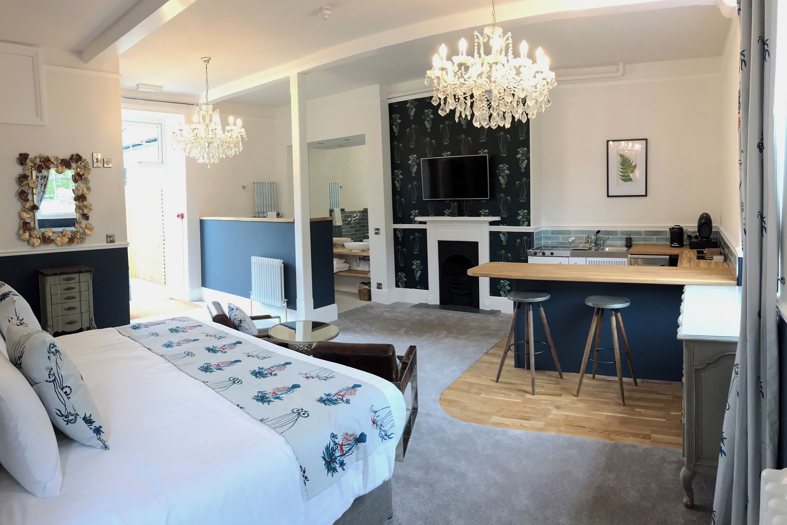 A modern bedroom with a large bed, a sitting area with a small table, and a kitchen with a bar.