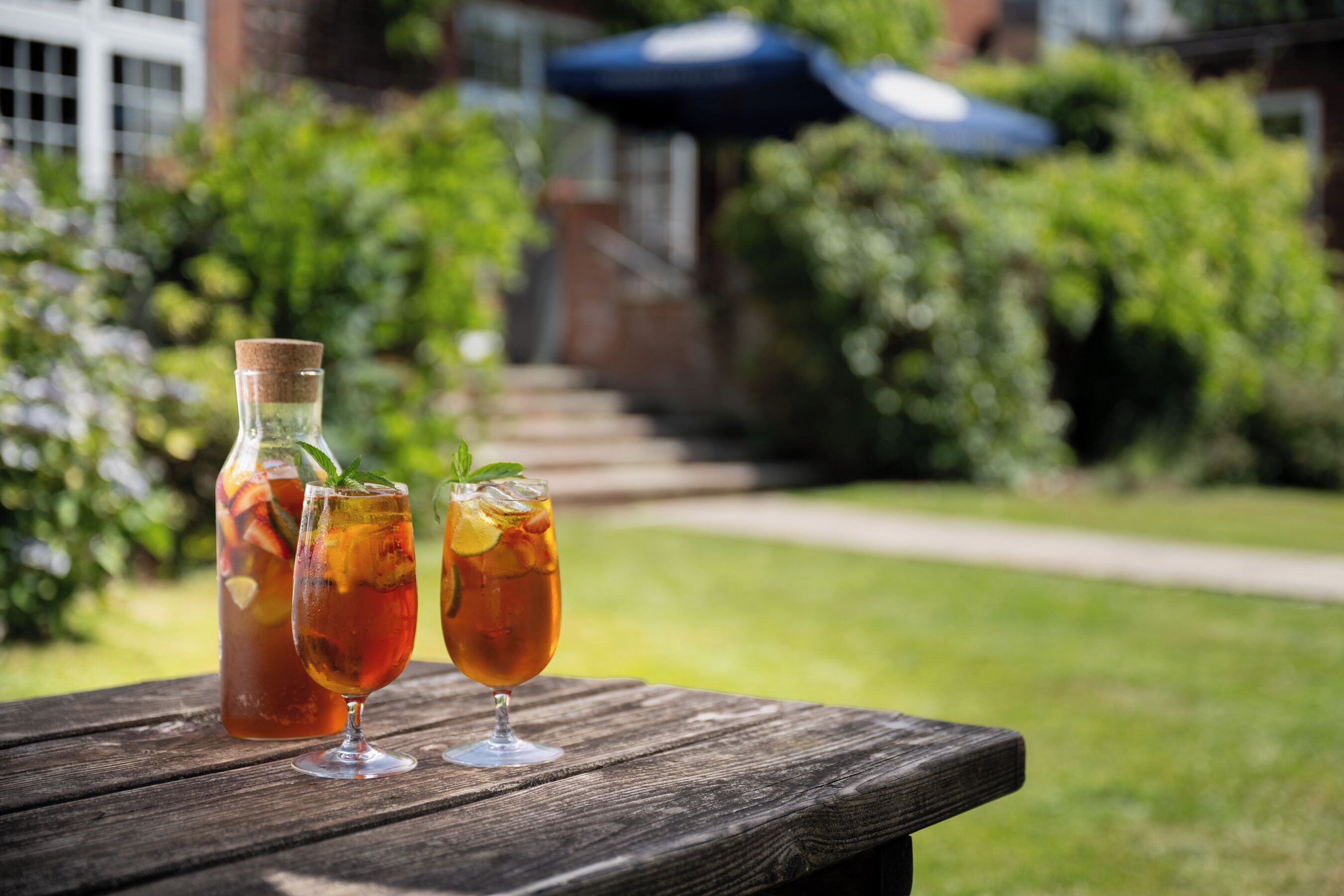 A wooden table with two glasses of iced tea and a bottle of water.