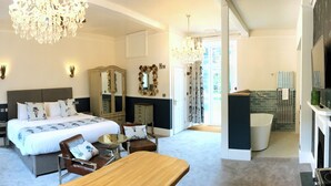 A bedroom with a bed, bedside tables, a mirror, a chandelier, and a view of the bathroom. - Fox & Hounds Country Hotel (Chulmleigh)