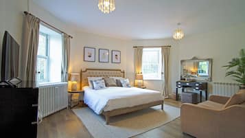 A bedroom with a bed, bedside lamps, a dresser, a chair, a desk, a mirror, and framed pictures on the wall.