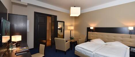 A hotel room with a large bed, two bedside tables, a desk with a chair, a TV, and a door.