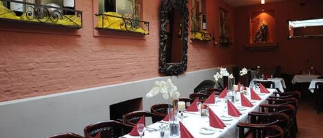 Un restaurante con mesas largas dispuestas para comer, una pared de ladrillo y una ventana con botellas.