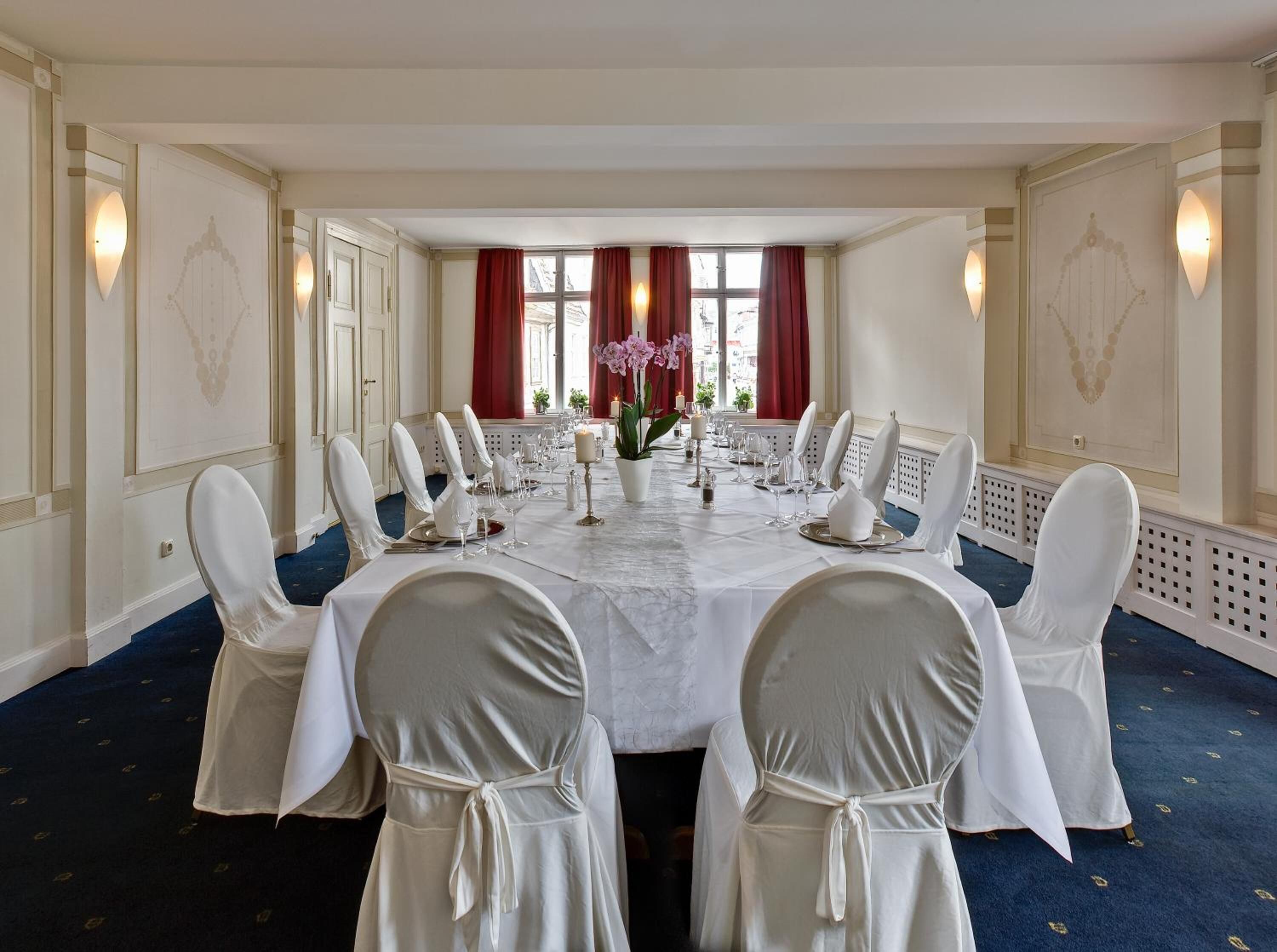 Un comedor formal con una larga mesa dispuesta para una comida, sillas blancas y decoración elegante.