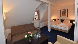 A hotel room with a sofa, a small table with a vase of flowers, a bed with pillows, and a framed picture on the wall. - Weinhaus Wöhler (Schwerin)