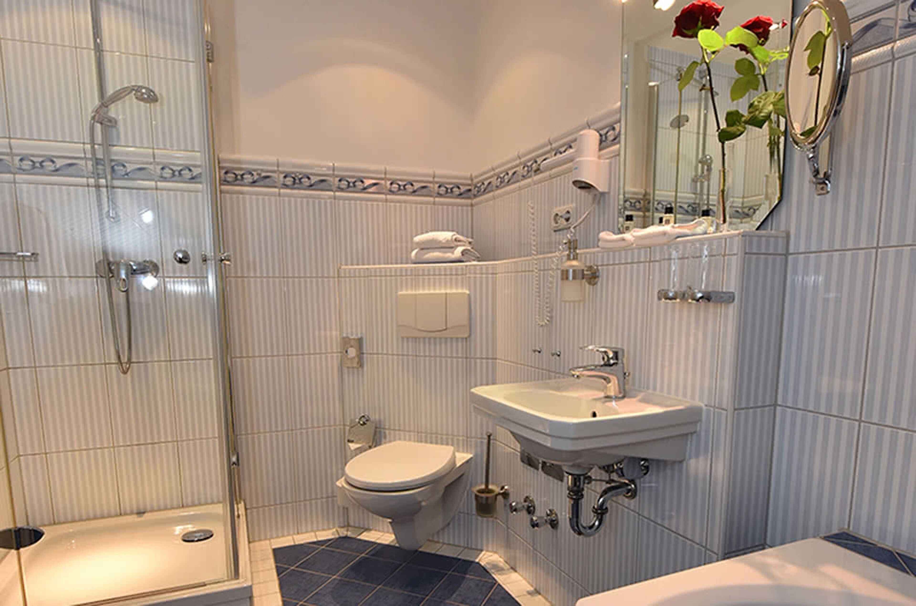 A bathroom with a shower, toilet, sink, and a mirror with a rose decoration.