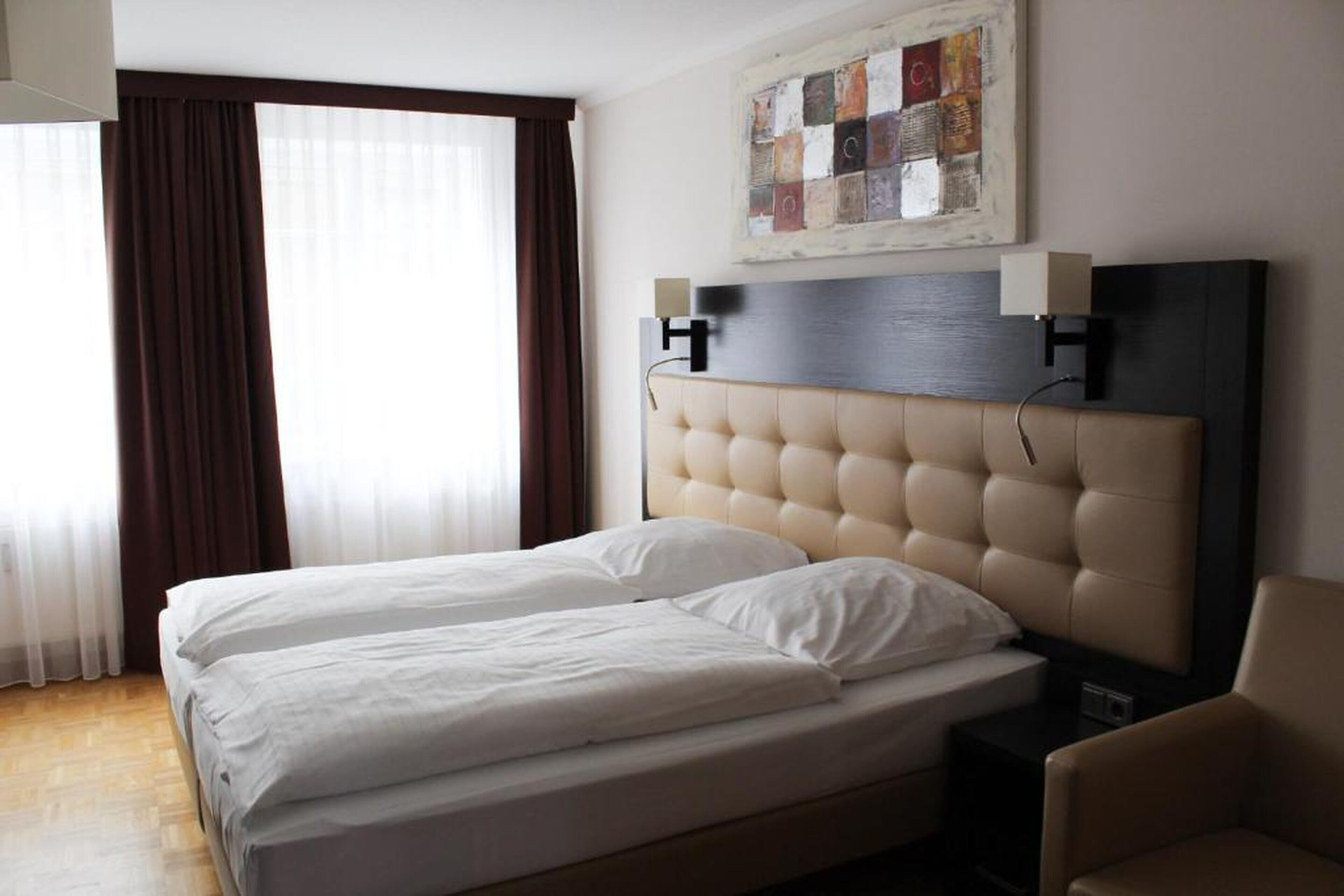 A hotel room with a large bed, two bedside tables, a chair, and a painting on the wall.