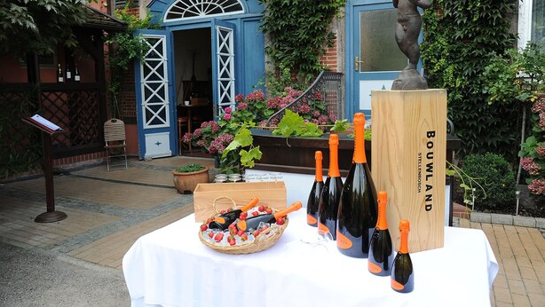 A table with bottles of wine and a basket of strawberries, set outdoors with a building in the background. - Weinhaus Wöhler (Schwerin)