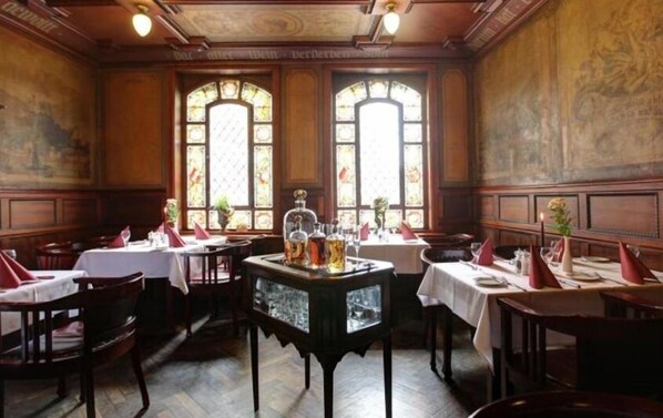 Un restaurante con paneles de madera, amplias ventanas arqueadas y mesas dispuestas para comer.