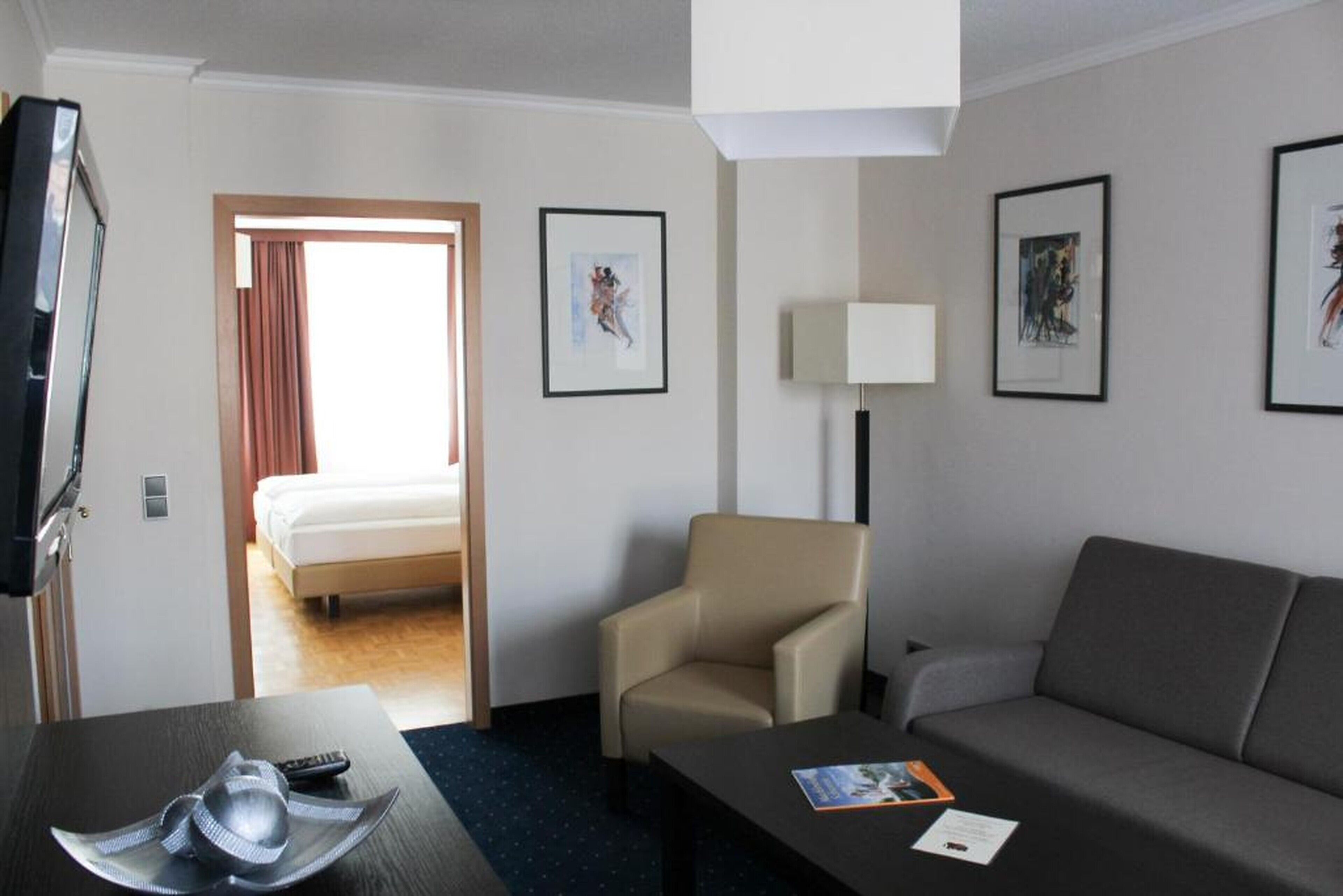 Une chambre d’hôtel comprenant un lit, un canapé, une chaise, un téléviseur et des œuvres d’art encadrées accrochées aux murs.