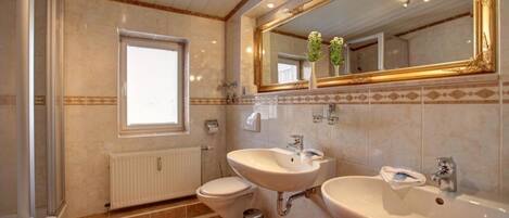 Un baño con inodoro, dos lavamanos, un espejo y una ventana.