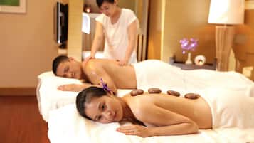 A spa setting with a massage table, a person receiving a back massage, and a massage therapist.