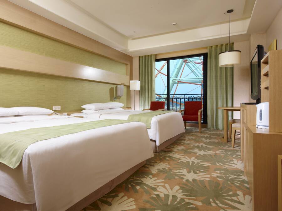 A hotel room with two beds, a desk, a chair, a TV, and a view of a Ferris wheel.