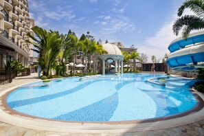 Una piscina grande y clara con un pabellón y palmeras, rodeada por un edificio de hotel.