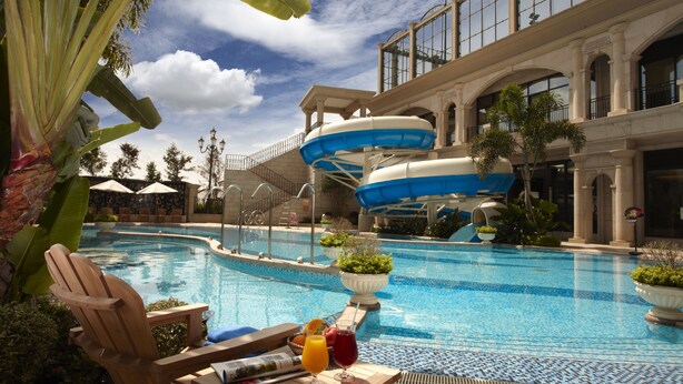A pool area with a water slide, lounge chairs, and a table with drinks. - E-Da Royal Hotel (Kaohsiung)