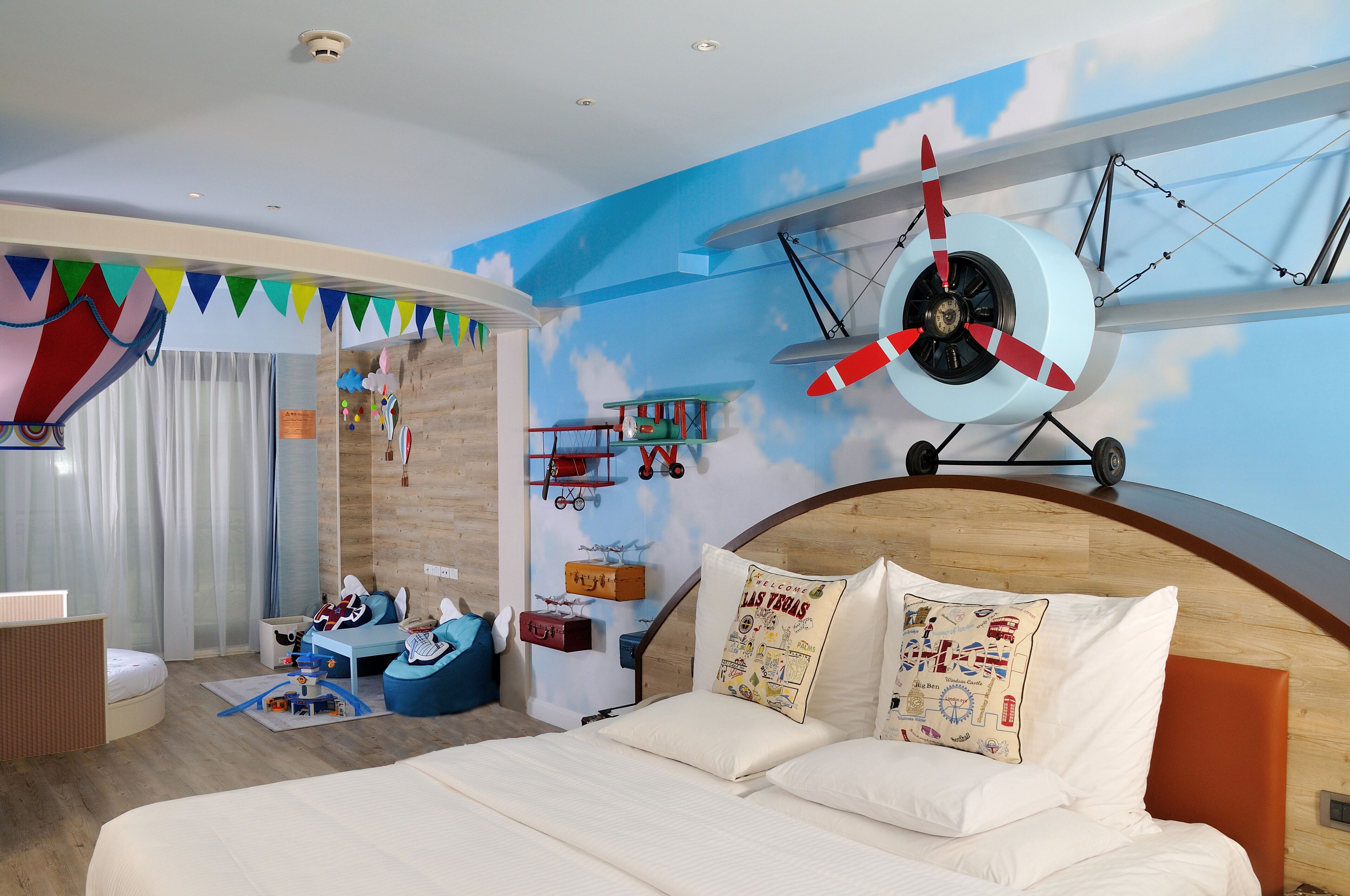 Un dormitorio con cama, cabecera de madera, mural de un avión y zona de juegos con juguetes.