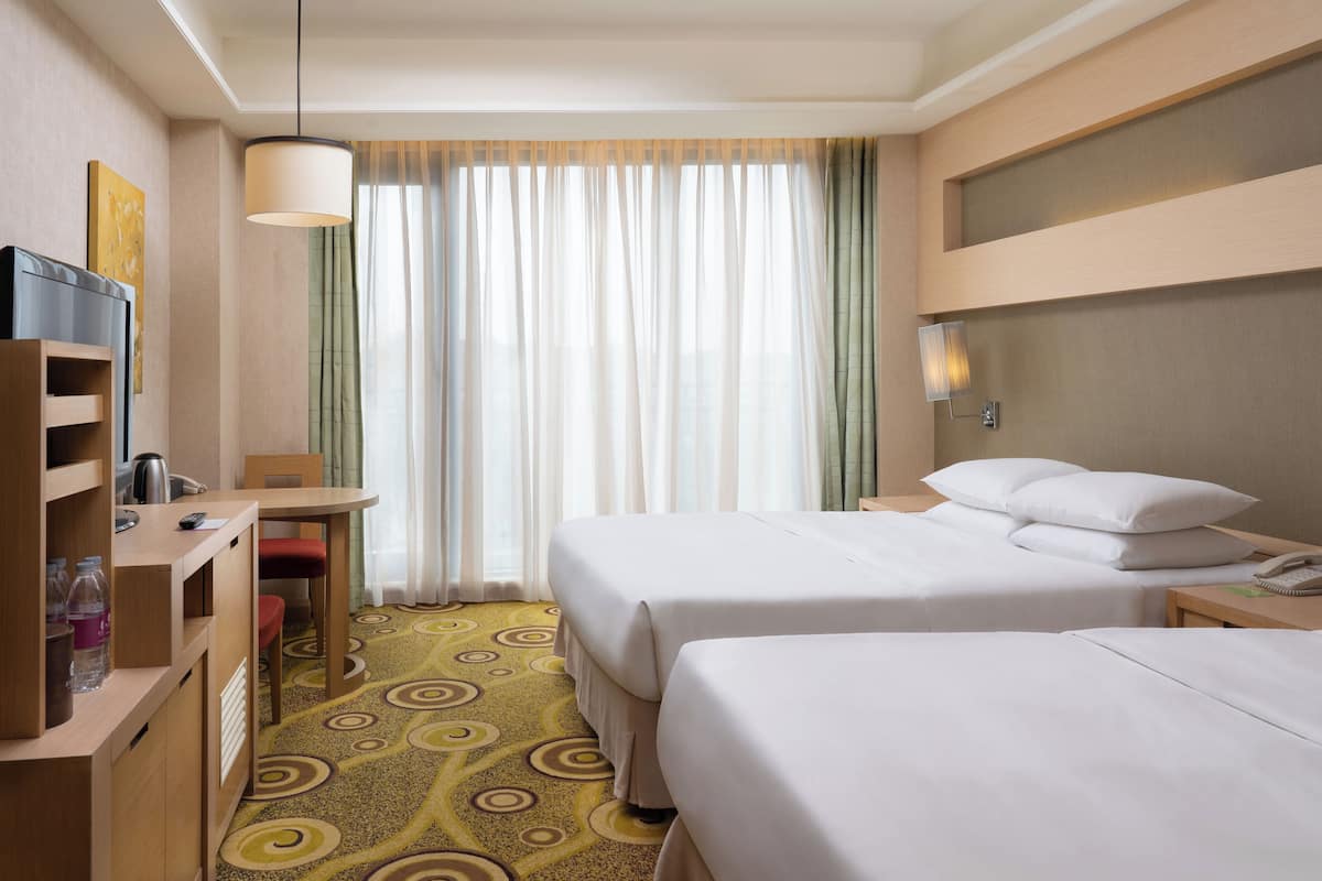 A hotel room with two beds, a desk with a chair, a TV, and a minibar.