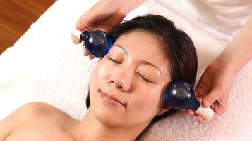 A person lying on a white towel with a massage device being applied to their head.
