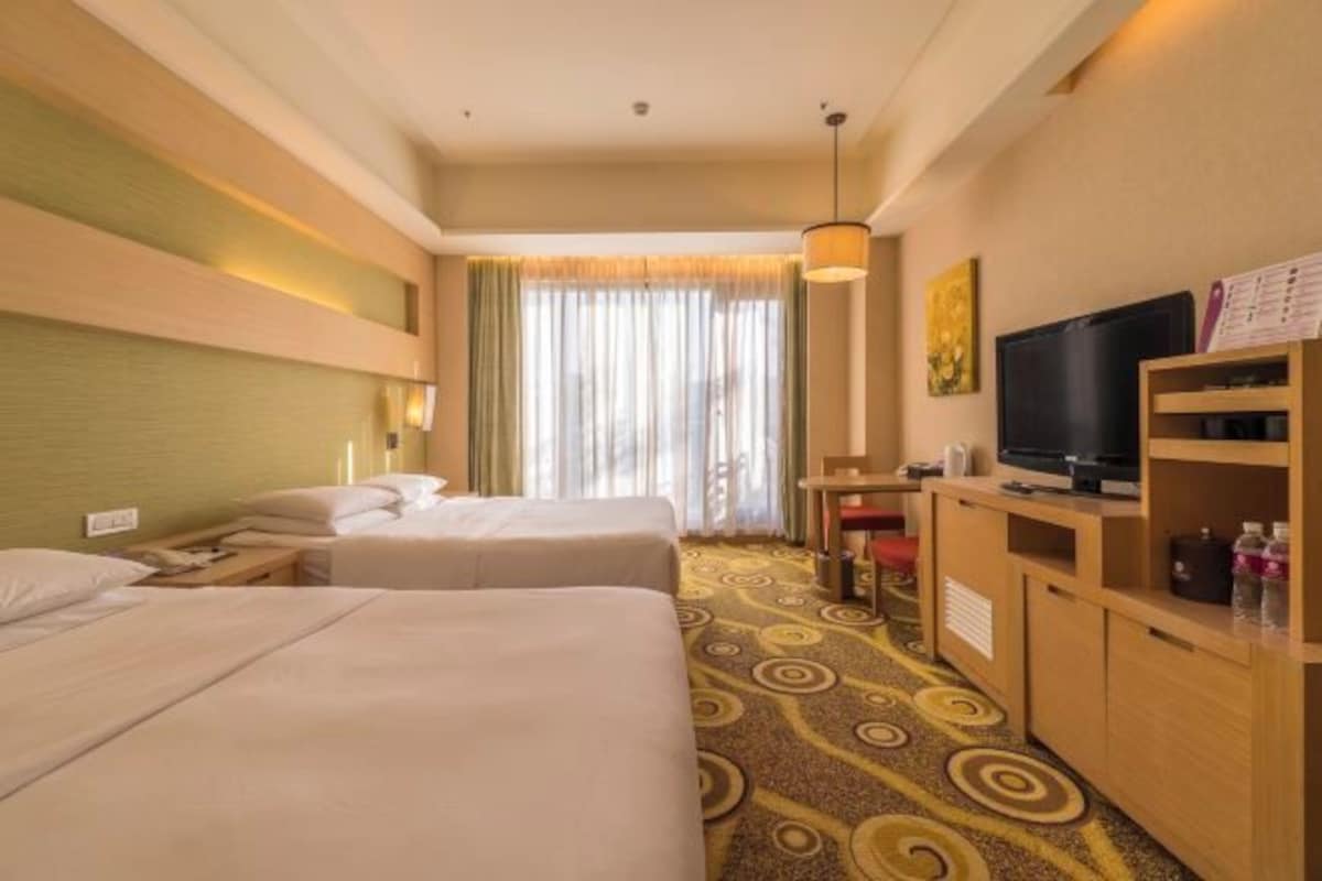 A hotel room with two beds, a TV, a desk, and a window with curtains.