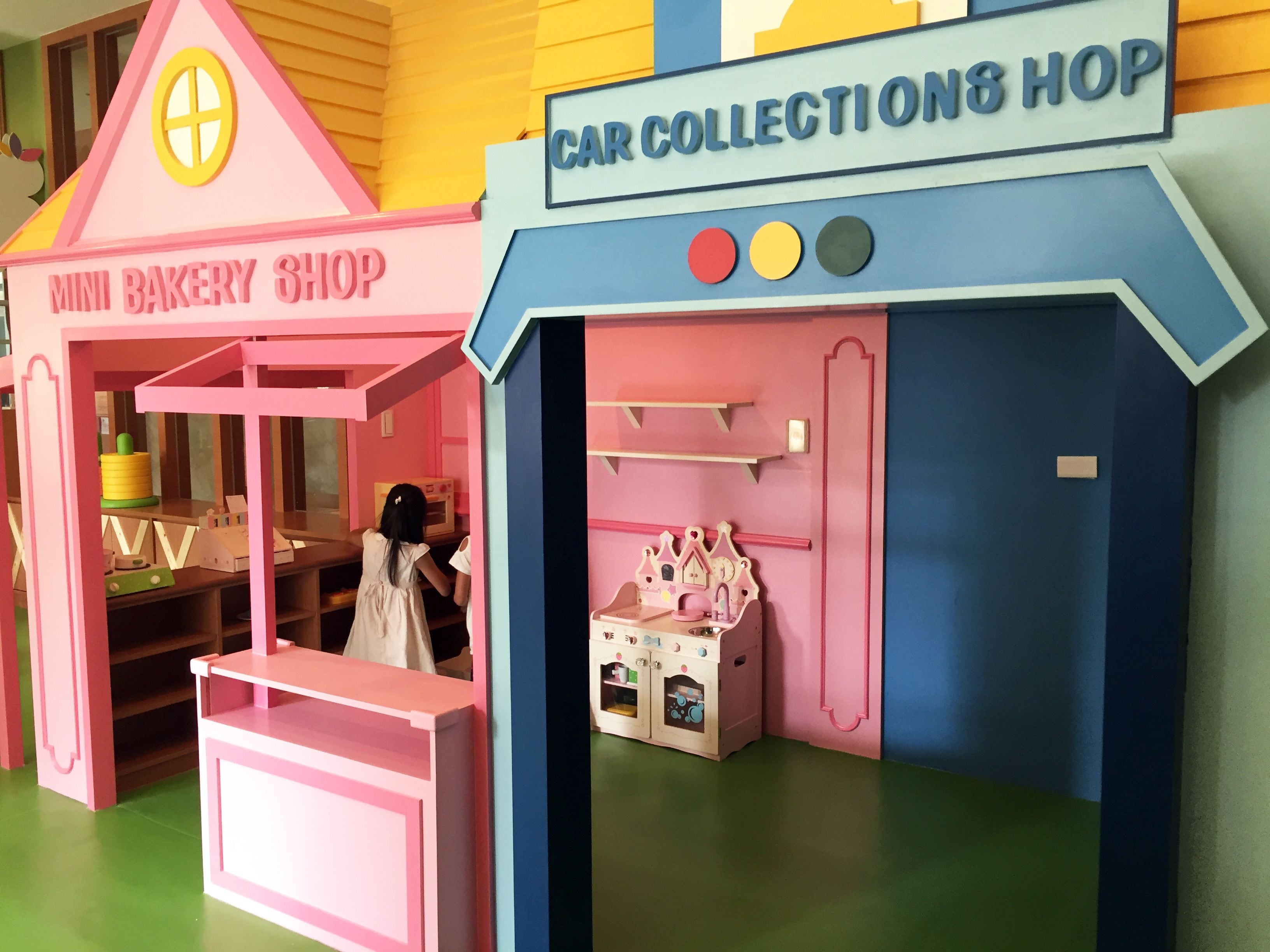Un espace de jeux coloré avec un petit magasin de pâtisserie et un espace dédié aux voitures miniatures.