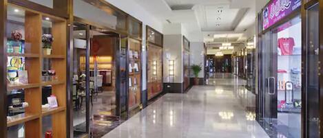 A corridor with glass-fronted shops, a polished floor, and a ceiling with recessed lighting.