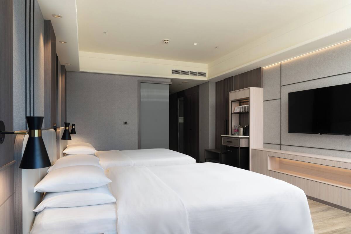 A modern hotel room with two beds, a flat-screen TV, and a minibar.