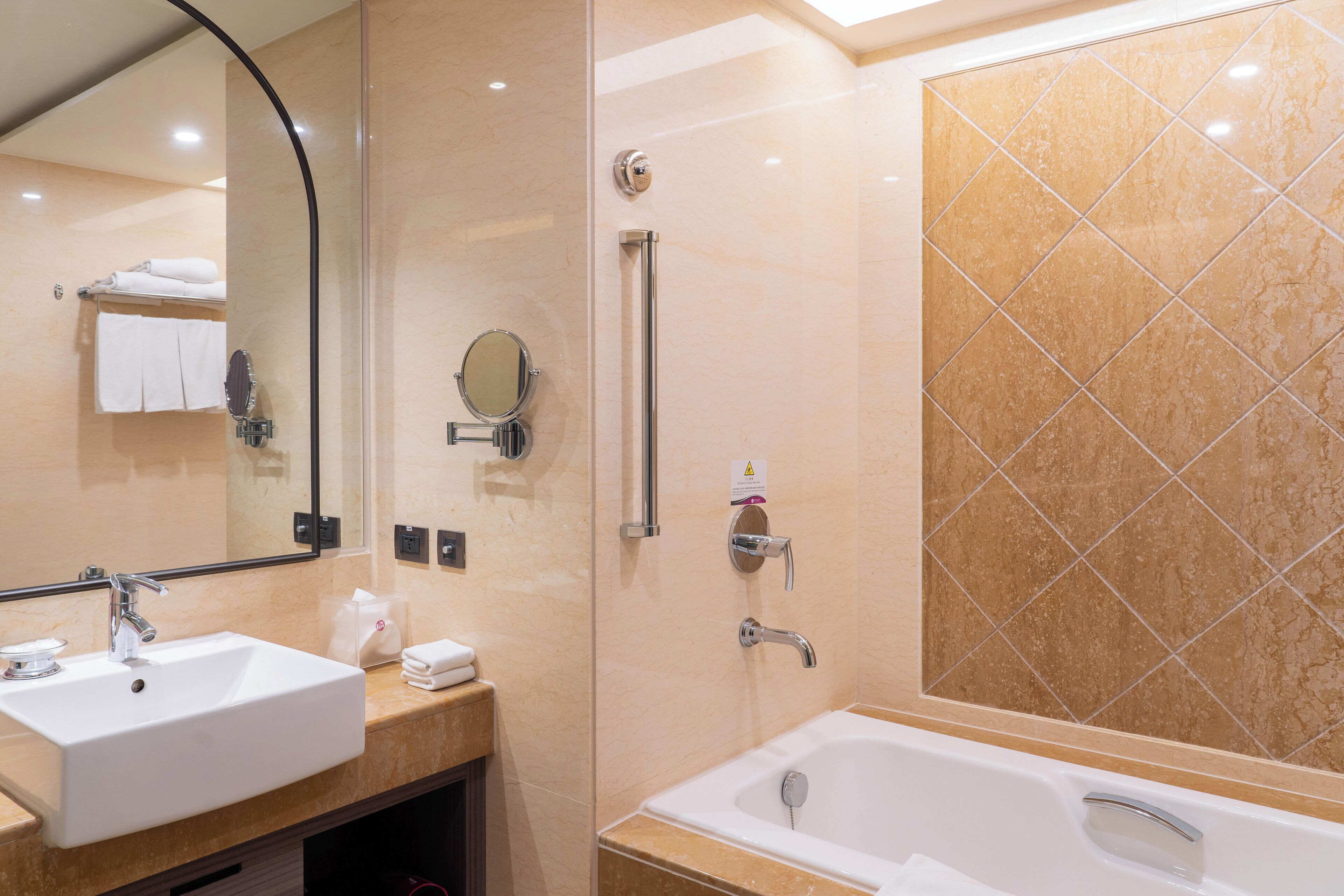 A modern bathroom with two sinks, a large mirror, a shower with grab bars, and a tiled wall.