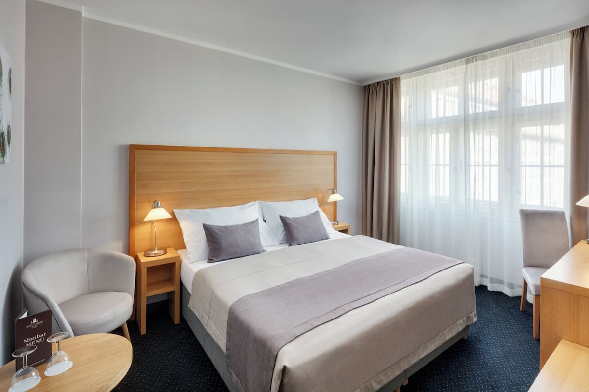 Una habitación de hotel con una cama grande, dos mesitas de noche con lámparas, una silla, un escritorio y una ventana con cortinas.