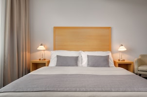 Uma cama bem arrumada com cabeceira de madeira, duas mesas de cabeceira com abajures e uma cadeira.