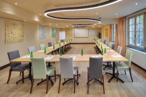 Sala de conferência com uma mesa comprida, cadeiras e tela de projeção.