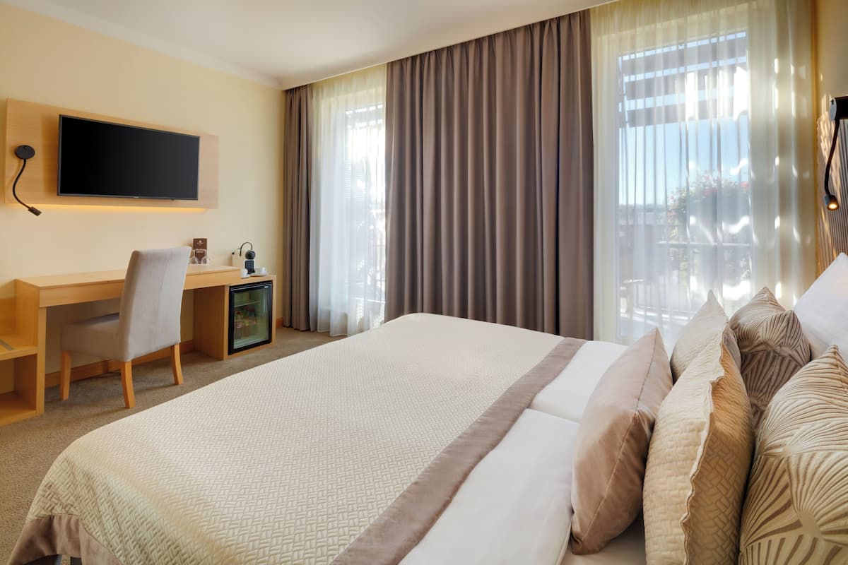 Habitación de hotel con cama, escritorio, silla, televisor y ventana con cortinas.