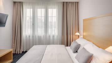 Ein Hotelzimmer mit einem großen Bett, einem an der Wand montierten Fernseher und einem Fenster mit transparenten Vorhängen.