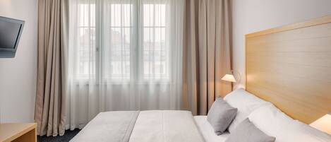 Una habitación de hotel con una cama grande, un televisor montado en la pared y una ventana con cortinas de gasa.