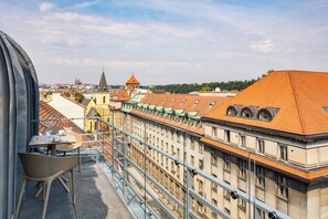 A balcony with a table and chairs, overlooking a cityscape with historic buildings and a church spire.