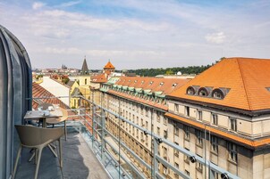 Uma varanda com mesa e cadeiras, com vista para um horizonte urbano com edifícios históricos e o topo de uma igreja.