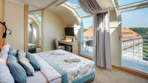 A modern hotel room with a large bed, a desk, a chair, a TV, and a balcony with a city view. - Hotel Clement (Prague)