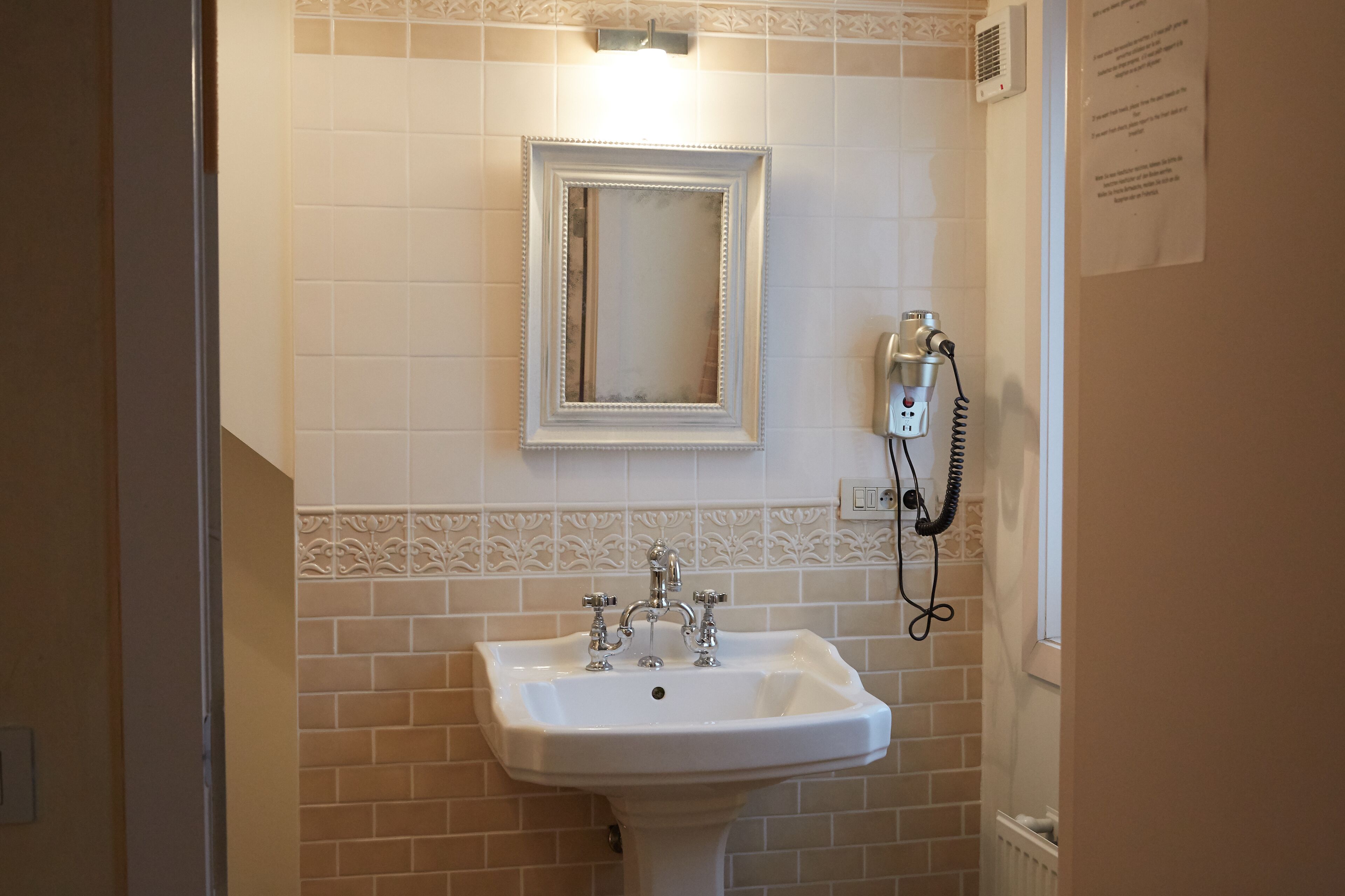 A bathroom with a white sink, a mirror, and a hairdryer on the wall.