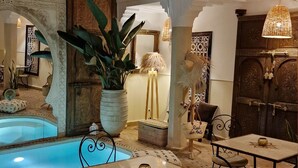 Un espace intérieur spacieux comprenant une piscine, une table à manger avec des chaises, ainsi que des éléments décoratifs tels que des plantes et des lampes.