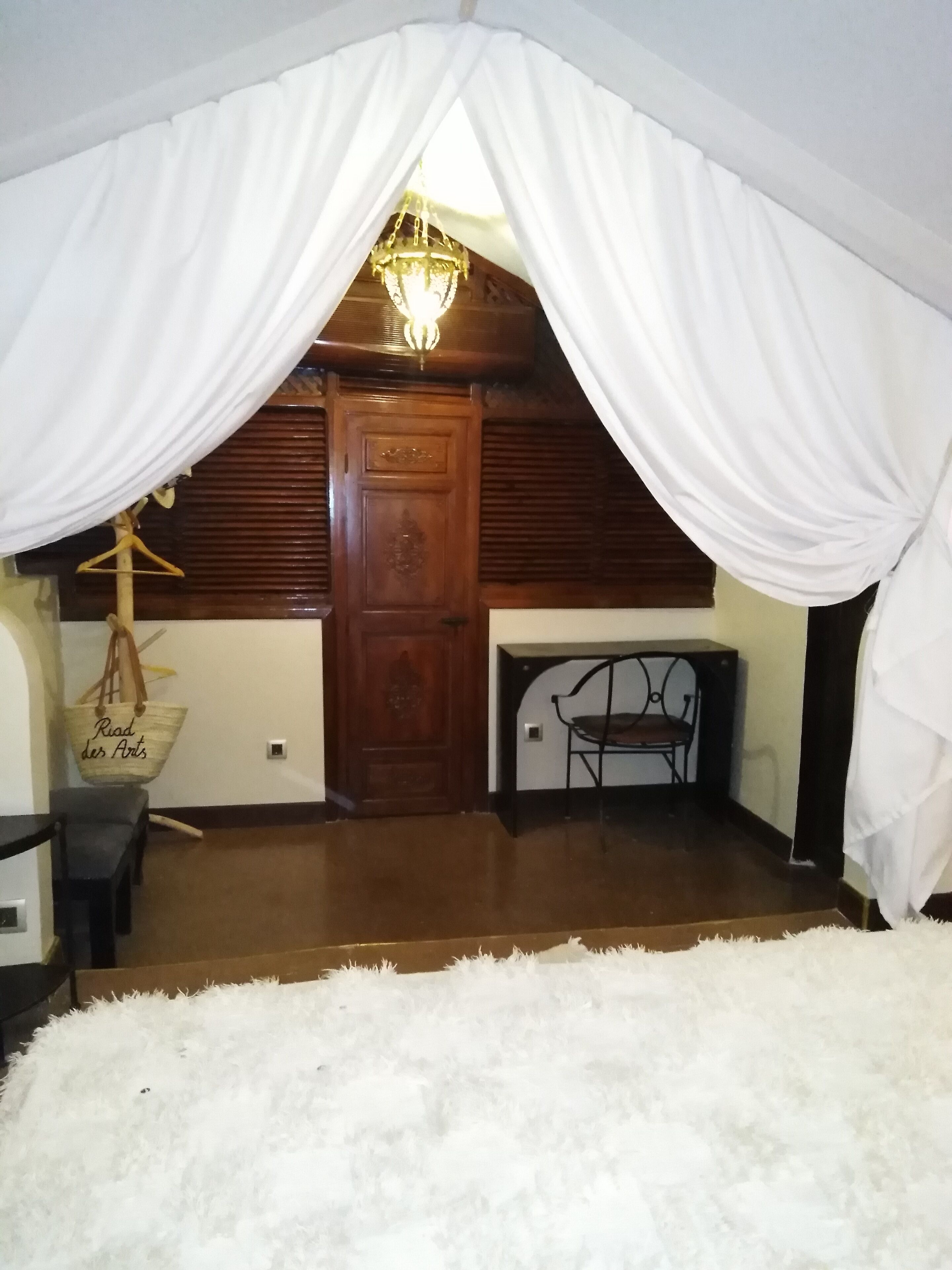A room with a wooden door, a hanging chair, and a white fur rug.