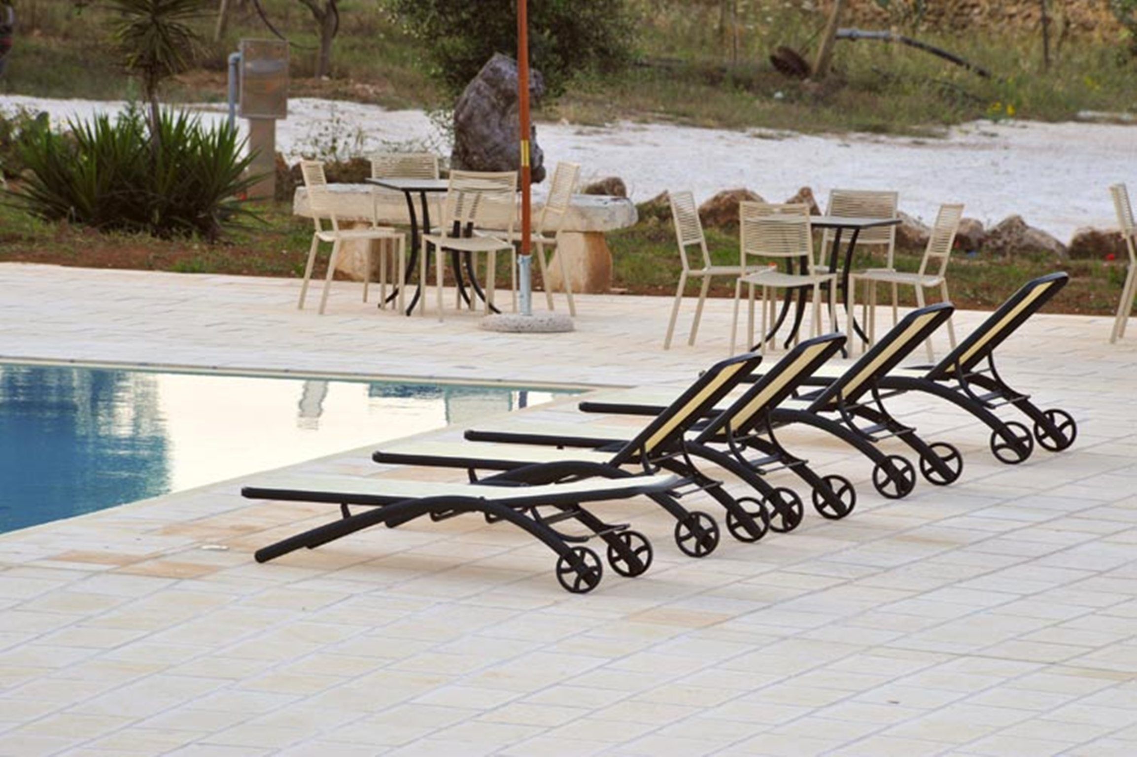 A poolside area with lounge chairs and a table, surrounded by a natural landscape.
