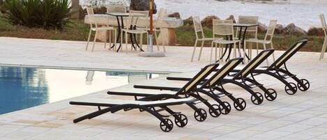 A poolside area with lounge chairs and a table, surrounded by a natural landscape.