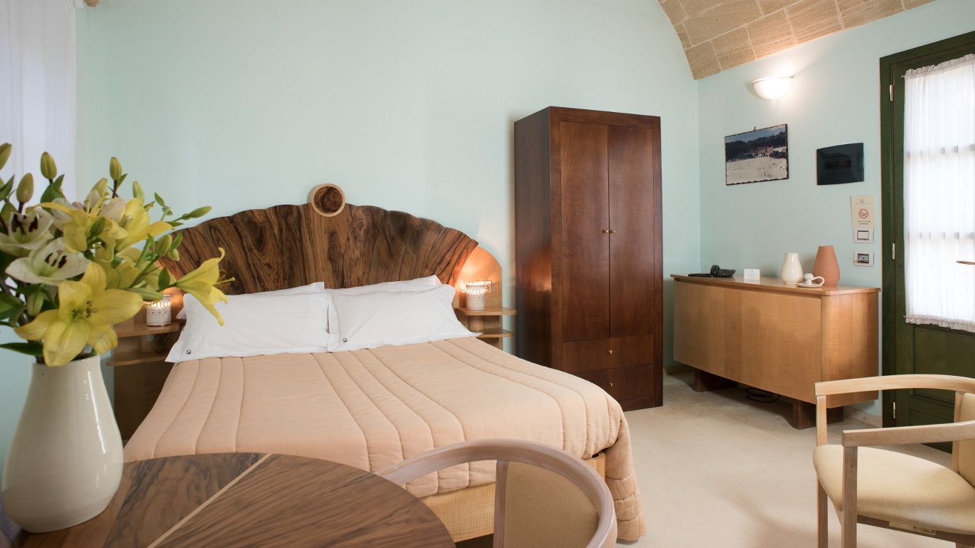 Un dormitorio con cama, mesita de noche, lámpara, armario de madera y un escritorio con silla.