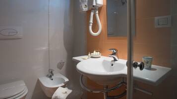 A bathroom with a white toilet, a bidet, a sink with toiletries, and a shower area.