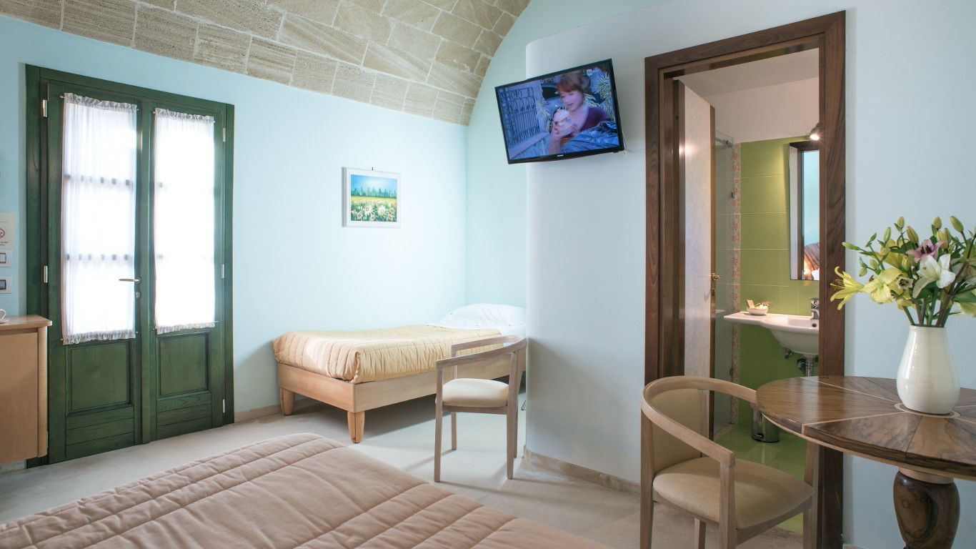 A bedroom with a bed, a chair, a TV, a picture on the wall, and a bathroom visible through an open door.