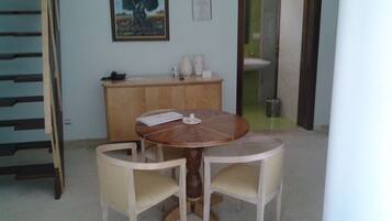 Un coin repas avec une table ronde en bois et deux chaises, un meuble en bois orné d’un vase et d’un téléphone, et un tableau représentant un arbre accroché au mur.