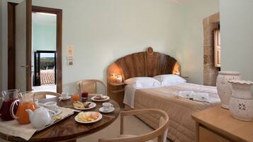 Una habitación de hotel con una cama, una mesa de desayuno, platos, vasos y una jarra de jugo de naranja.