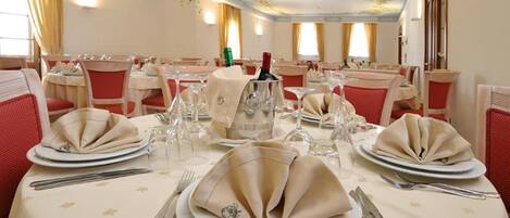 Une salle de banquet avec des tables rondes dressées pour le repas, chacune agrémentée de serviettes pliées, de couverts et de verres à vin.