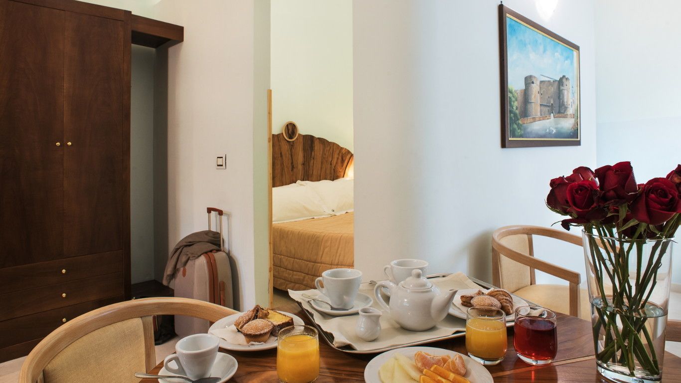 A hotel room with a bed, breakfast tray, and a vase of red roses.