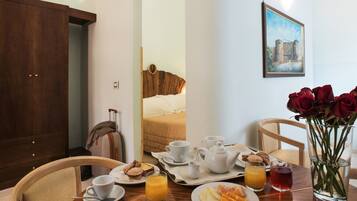 A hotel room with a bed, breakfast tray, and a vase of red roses.