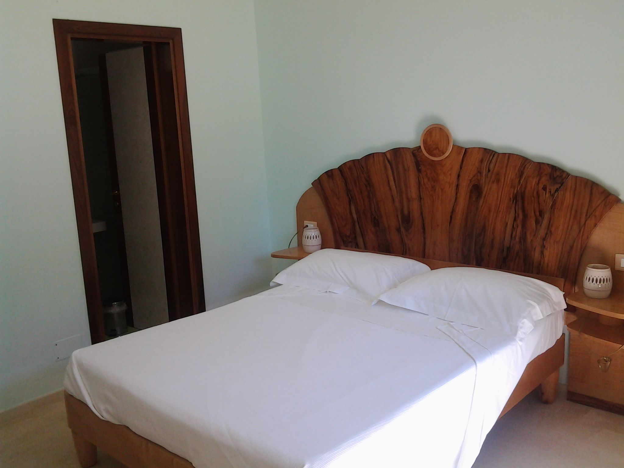 A neatly made bed with white linens, a wooden headboard, and a bedside table with a lamp.